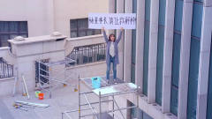 女孩想董事长解释，举着牌子站在铁架子上，脚