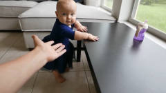 宝宝正扶着椅子站着，忽然宝妈向宝宝伸出手，